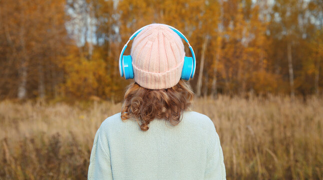 Inspired young woman enjoying listening to music in headphones outdoors in autumn forest