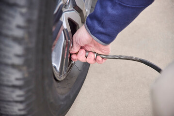 Unrecognizable person checking the air in their car tires and inflating them. Close up view.