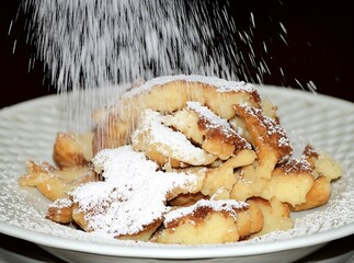 Fluffy Kaiserschmarrn, a traditional Austrian shredded pancake, is artfully dusted with fine powdered sugar, creating a delightful dessert presentation.