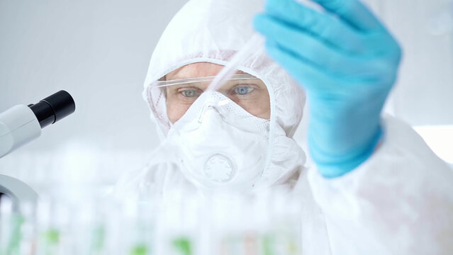 Professional scientist in protective gear is using pipette and examining a test tube in a laboratory setting