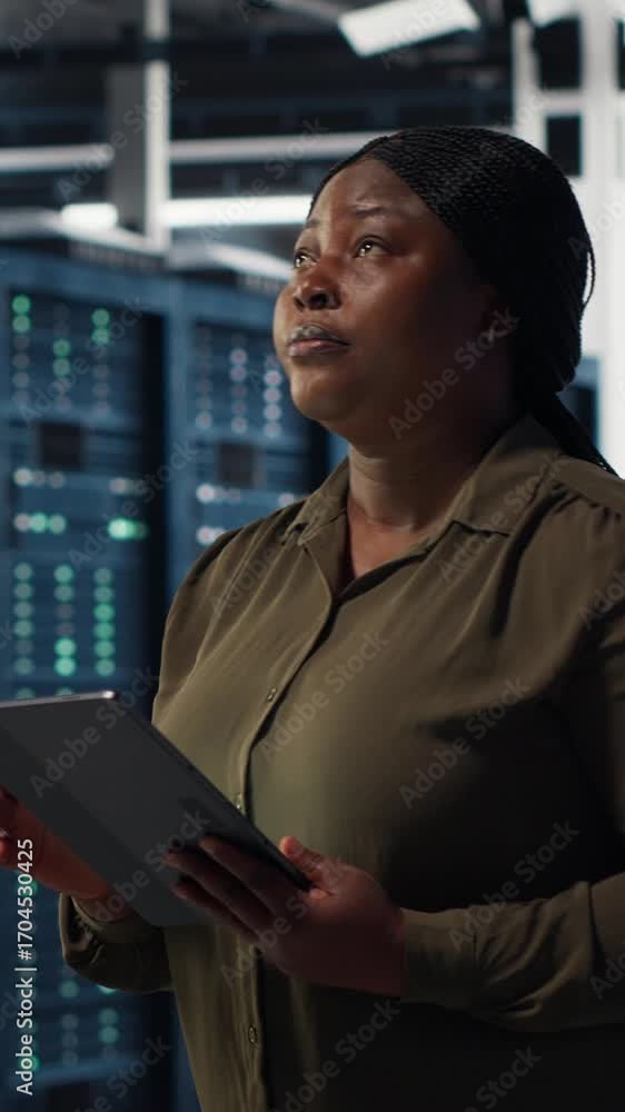Poster vertical video engineer with tablet walks through data center server rows, implementing advanced pow