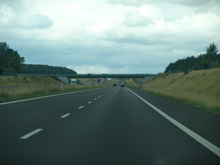 Multi-lane highway under cloudy skies with cars in motion, grassy median, and forested surroundings—modern road infrastructure in a natural setting.