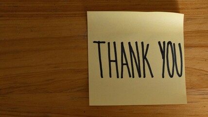 Obraz premium Yellow sticky note with handwritten THANK YOU on wooden surface, ideal for gratitude, appreciation, and personal communication design themes