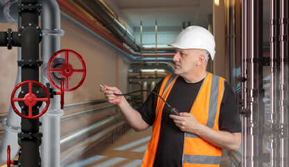Technician in safety vest and helmet inspects industrial pipeline with red valves using diagnostic device. Maintenance, engineering control, and safety check of fluid systems.