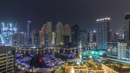 Fototapeta premium Yachts in Dubai Marina flanked by the Al Rahim Mosque and residential towers and skyscrapers aerial night timelapse.