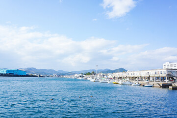 静かな港と青い海、山々と漁船が並ぶ風景