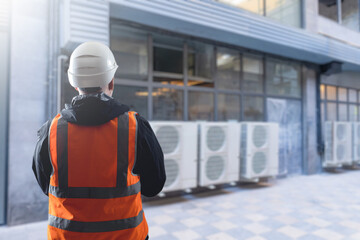 Engineer in safety vest and helmet inspecting outdoor air conditioning units, HVAC installation,...