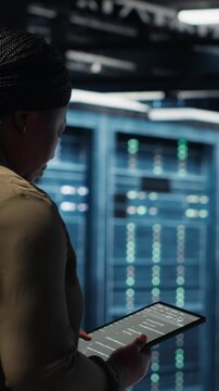 Vertical video Close up of data center programmer doing data analysis on tablet to upgrade infrastructure. African american woman in server room using device to manage storage systems datasets