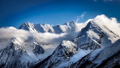 Obraz premium A Mountain Range Covered In Clouds And Snow The Sky Is Blue And The Clouds Are White The Mountain Range Is Very Tall And Majestic