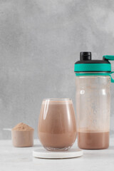 Chocolate protein shake with powder and shaker bottle on a light gray background