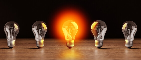 Concept of idea. One glowing light bulb among others on wooden table against black background....