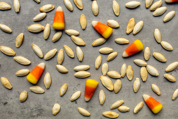 close-up of scattered roasted pumpkin seeds and bright colored candy corns scattered against a gray backdrop in a horizontal orientation, Halloween themed
