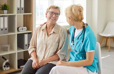 Friendly conversation of nurse and senior woman, consultation for elderly patient in clinic. Doctor with stethoscope hugging old lady and talking good news, smiling people sitting on chairs
