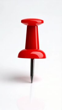 Close up of a shiny red pushpin standing upright on a bright white surface, reflecting light and showing sharp point.