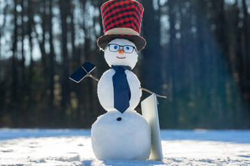 Fototapeta premium Businessman snowman talking on smartphone in winter. Snowman making a business phone call. Funny snowman hacker using laptop outdoors. Snowman with mobile phone during winter holiday.
