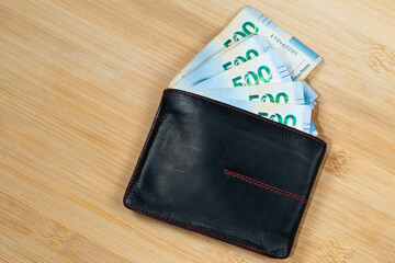 a leather wallet with mexican money inside over a wooden background