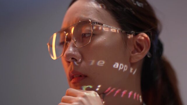 A young woman in a hoodie works on her computer in a dark room. Lines of code from the screen are projected onto her face, showing her deep focus on future technology.
(158 characters)