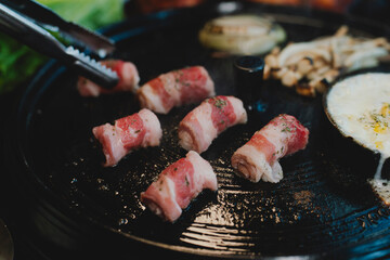 Sizzling Korean BBQ pork belly (samgyeopsal) on tabletop charcoal grill with rising smoke and...