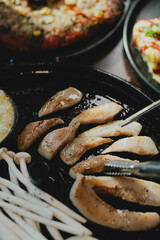 Sizzling Korean BBQ pork belly (samgyeopsal) on tabletop charcoal grill with rising smoke and traditional banchan side dishes, close-up shot in cozy restaurant setting with copy space.