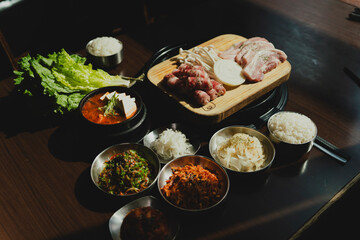 Sizzling Korean BBQ pork belly (samgyeopsal) on tabletop charcoal grill with rising smoke and traditional banchan side dishes, close-up shot in cozy restaurant setting with copy space.