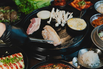 Sizzling Korean BBQ pork belly (samgyeopsal) on tabletop charcoal grill with rising smoke and traditional banchan side dishes, close-up shot in cozy restaurant setting with copy space.