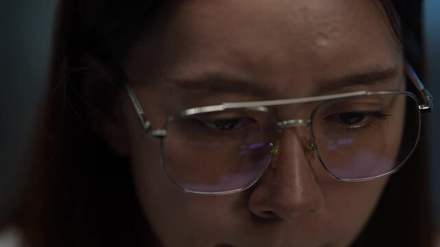 An extreme close-up of a young woman's glasses reflecting computer code. She is working late at night, focused on a complex technology problem on her screen.