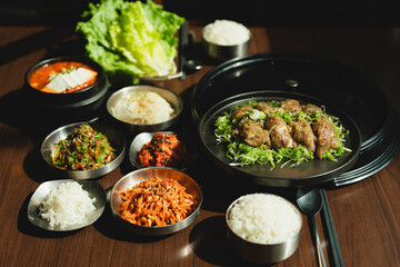 Sizzling Korean BBQ pork belly (samgyeopsal) on tabletop charcoal grill with rising smoke and traditional banchan side dishes, close-up shot in cozy restaurant setting with copy space.