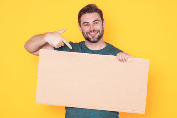Happy man with blank banner isolated on studio background. Portrait of attractive man with empty blank poster. Man showing poster, pointing finger on signboard placard. Billboard or banner concept.