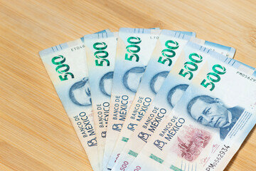 a six mexican bills of five hundred pesos at the right corner over a wooden background