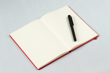 a red blanked notebook with a black pen over its right sheets and a white background