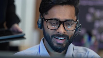 A smiling male customer support agent assists a client from his computer workstation. He works in a modern call center, providing professional and positive online assistance. - Powered by Adobe