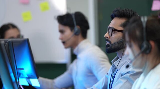 A diverse team of customer support agents works in a modern call center office. The operators are busy assisting clients over the phone with their questions and technical problems.