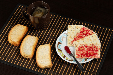 Close up to a Salt cookies spread with red fruits jam and a tea cup with toast over a wooden table place mat