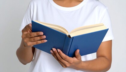 Mid-section of person holding open book with blue cover. Person wears white t-shirt. Light background highlights pages