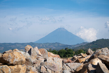 Photograph of a volcano with large rocks in the foreground taken on a sunny day