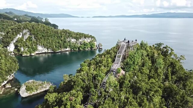 Drone view of Marindal Peak in Raja Ampat, Indonesia, featuring lush islands, turquoise sea, and a scenic wooden viewing deck above the ocean.