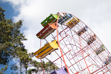 Photograph of a color wheel, a handmade mechanical ride in Central America, with people sitting in...