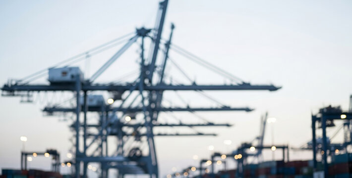 Cranes stand tall at a bustling port with a blurred industrial background and a soft light sky, symbolizing global trade, structure, and scale.