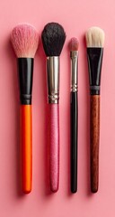 Four makeup brushes in various colors against a pink background