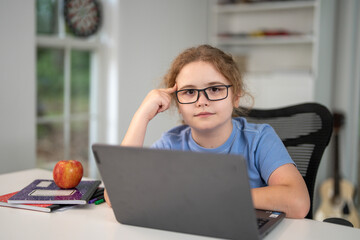 Kid learning at home with laptop and books. Child learn online using laptop at desk. Learning with homework in child room. E-learning on laptop. Kid learning at home. Interior with kid and laptop.