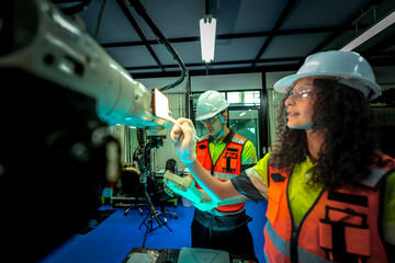 maintenance engineers troubleshoot an electrical control cabinet. They are diagnosing a fault in the system by cross-referencing the wiring with a digital schematic on a tablet.