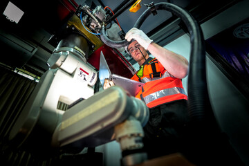 maintenance engineers troubleshoot an electrical control cabinet. They are diagnosing a fault in the system by cross-referencing the wiring with a digital schematic on a tablet.