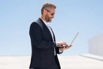 Business man using laptop outdoors. 40s man using laptop. Confident business man with laptop. Business online. businessman checking data on laptop outside. Business man in suit work online.