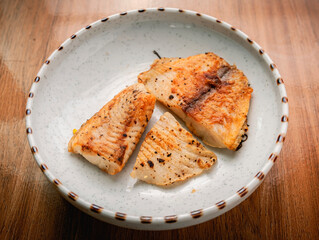 Grilled fish pieces placed on a white ceramic plate on a wooden background.