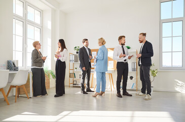 In modern office environment, several diverse groups of professionals interact during workday. People are dressed in business attire and engage in lively discussions, exchanging ideas and opinions.