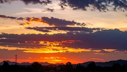 Fototapeta premium Vibrant sunset over silhouetted landscape with dramatic clouds.