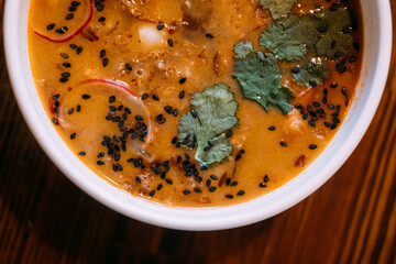 Sesame soup. Hot meal. Orange broth served with vegetable greens in bowl on wooden table. Tasty aromatic spicy dining food with radish.