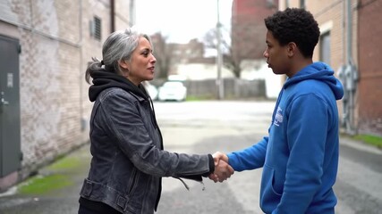 Intergenerational handshake signifying mentorship and agreement between a senior woman and a young man in a city alley