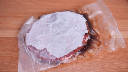 close-up of vacuum-sealed frozen beef burger patty on wooden surface.