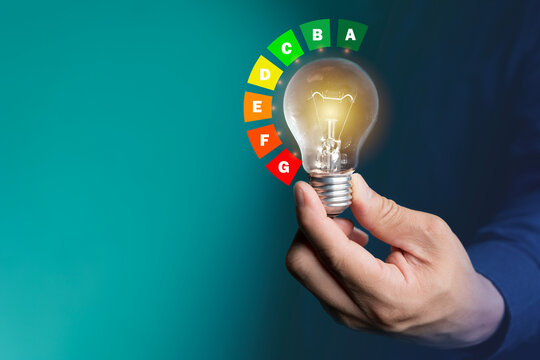 Hand holding glowing light bulb with colorful energy efficiency rating chart concept of power saving idea
